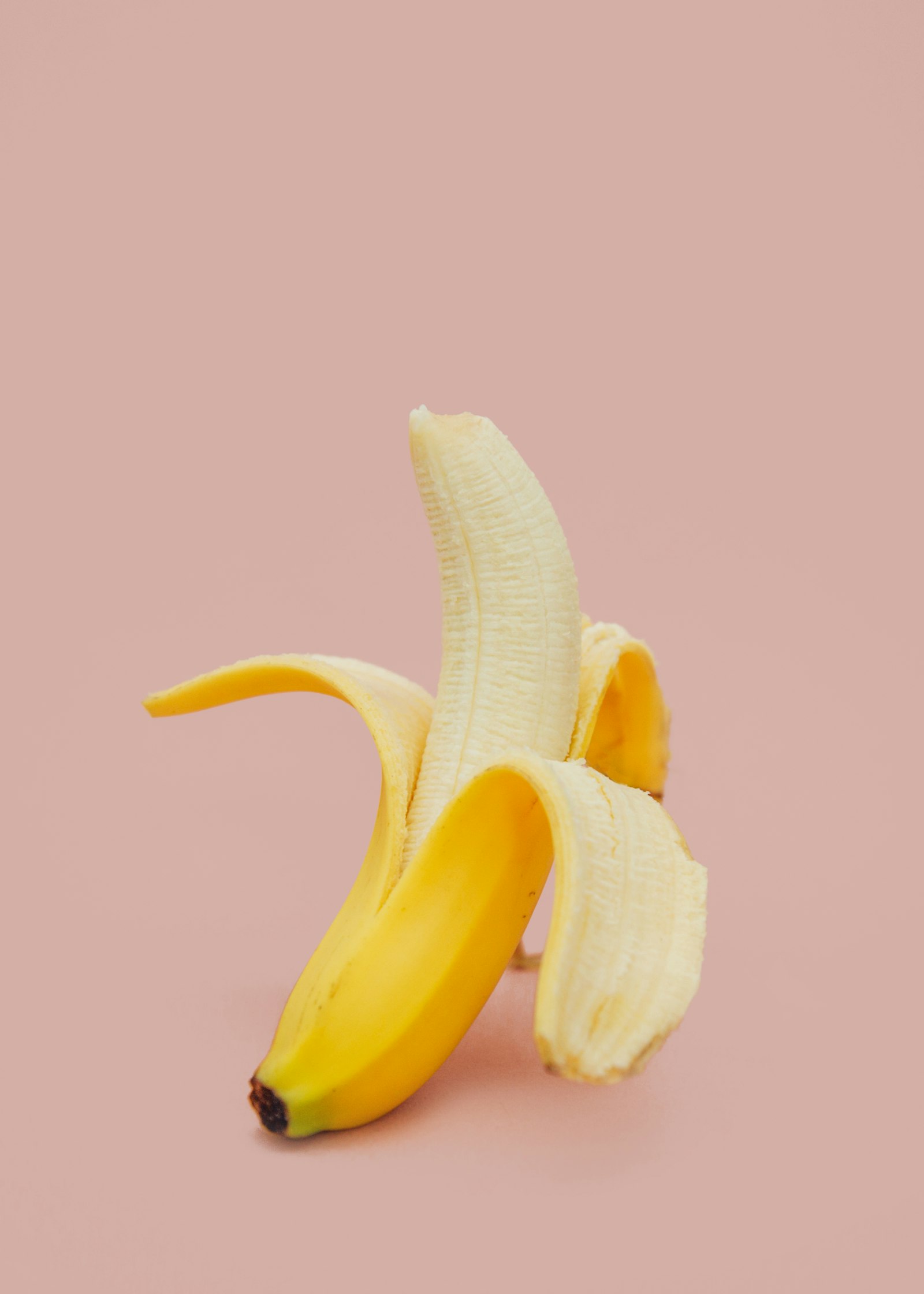 A half-peeled banana on a pink background